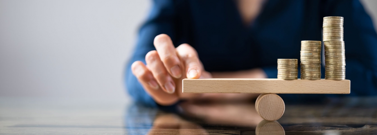 Een evenwichtsbalk met aan de rechterkant een stapel geld en aan de linkerkant een hand die de evenwichtsbalk vasthoudt