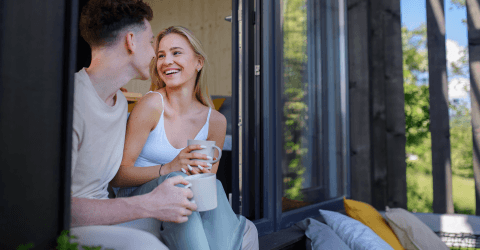 Jong stel drinkt in de deuropening van hun nieuwe huis koffie en knuffelenuffel